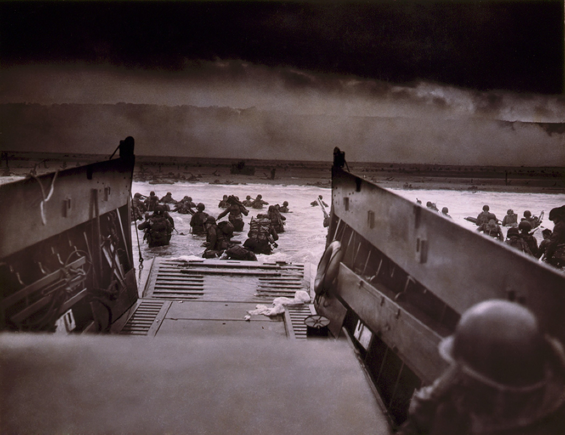 American soldiers wade from Coast Guard landing craft toward the Omaha Beach against machine gun fire on D-Day. June 6, 1944, by Coast Guard photographer, Robert F. Sargent.